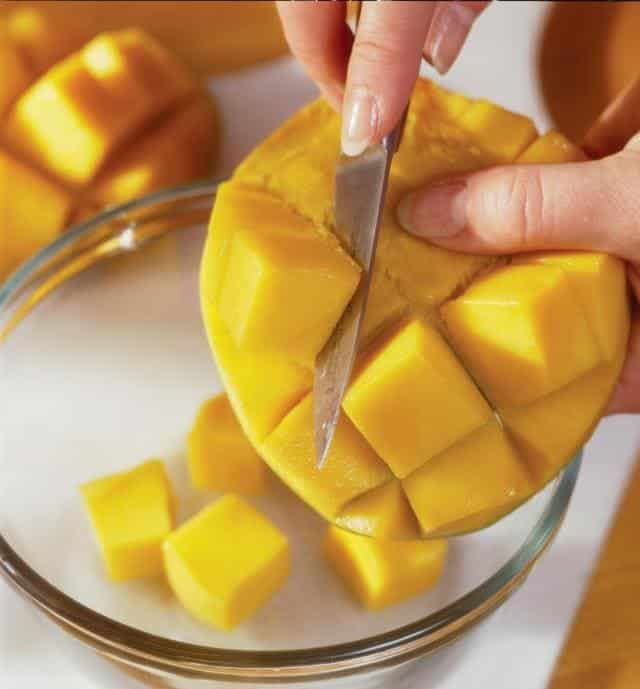 A person taking out mango flesh with a knife