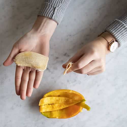 A top view of a hand holding a mango seed taking out all its skin