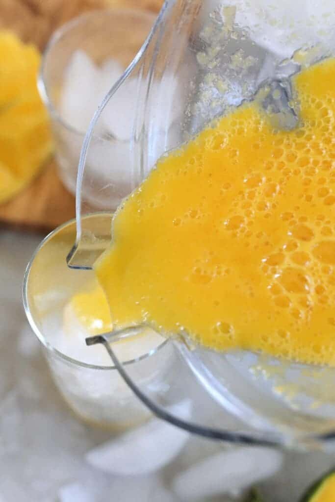 A top view of a mango juice being poured into a glass from blender