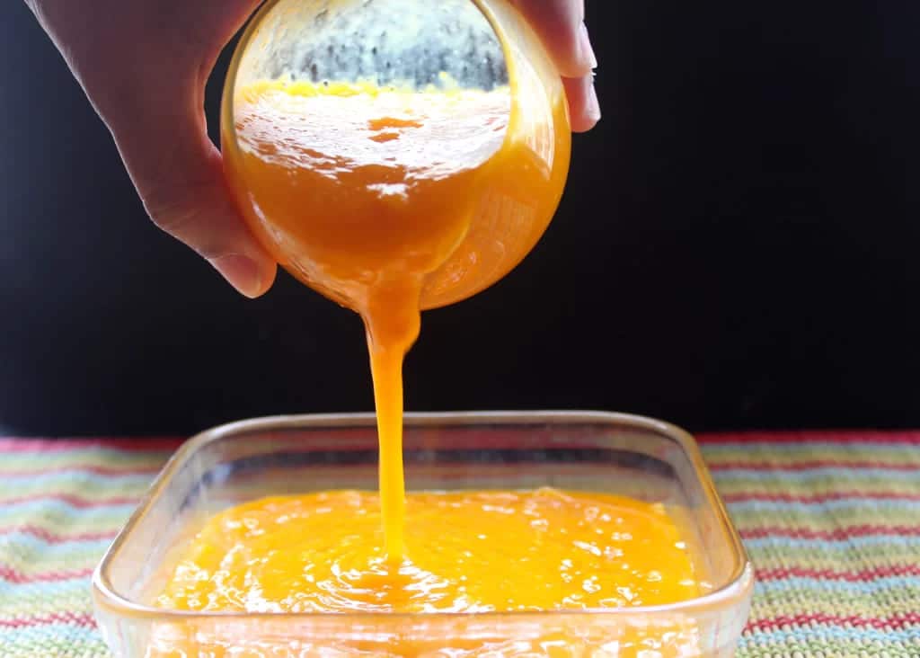 A view of thick mango puree being poured into a glass tray for storage