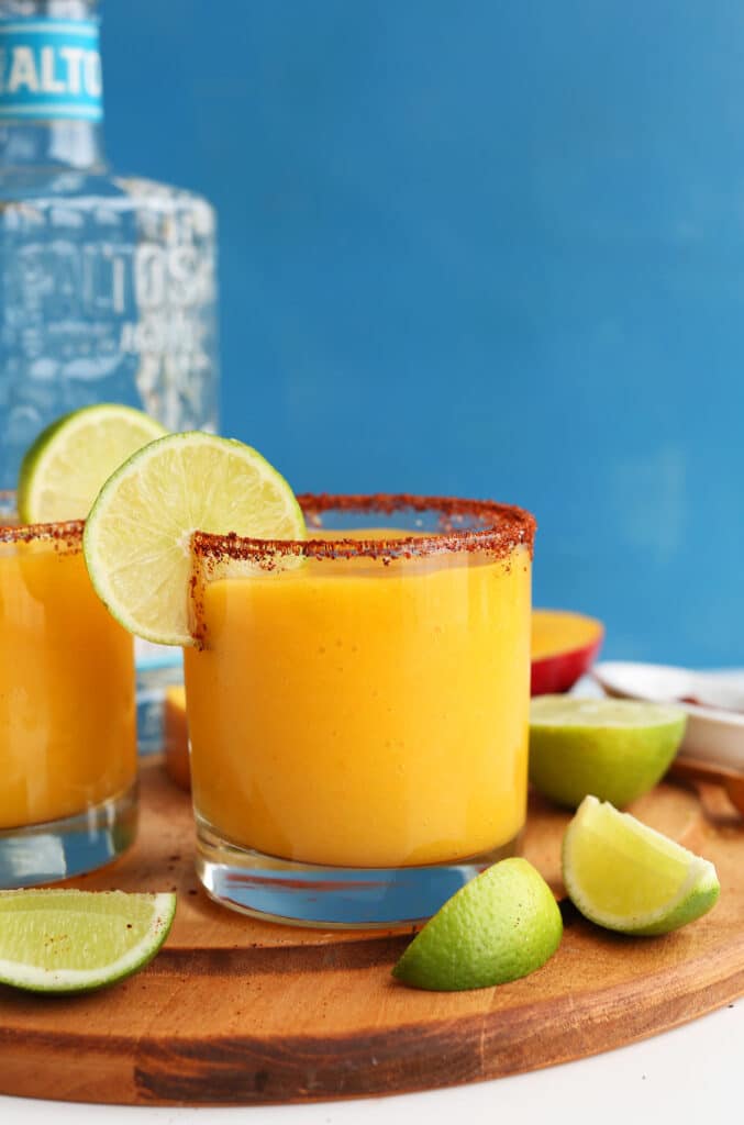 Mango Chili Lime Margaritas served in rim glasses placed on a wooden board with lemon wedges