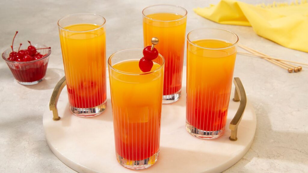 four glasses of mango tequila sunrise garnished with cherries