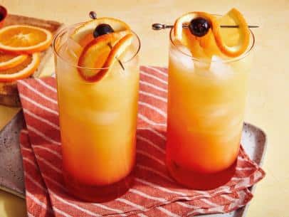 mango tequila sunrise served in two glasses with cheery and oranges as garnish