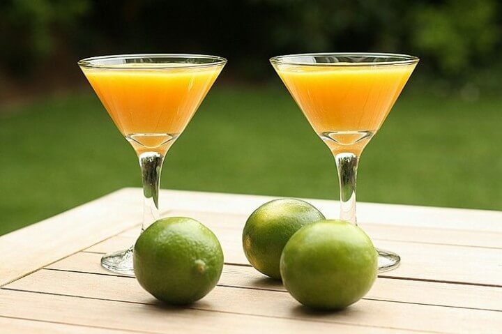 two glasses of mango martini with three lemons lying in front