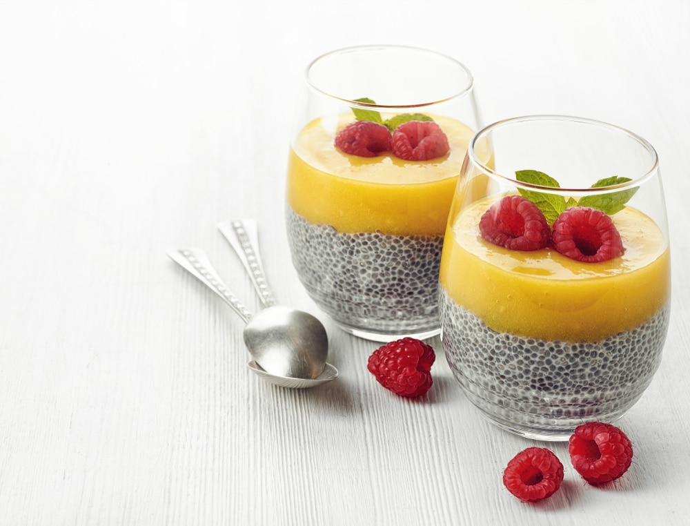 Healthy vegan chia pudding with mango sauce and fresh raspberries on white wooden background