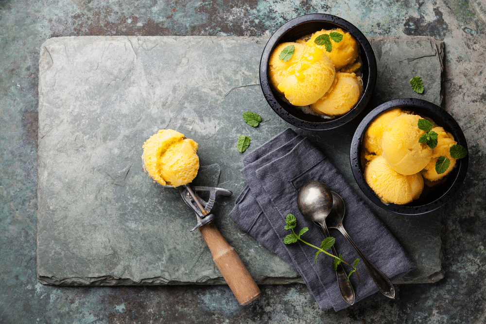 Mango ice cream sorbet with mint leaves and Spoon for ice cream on stone slate background