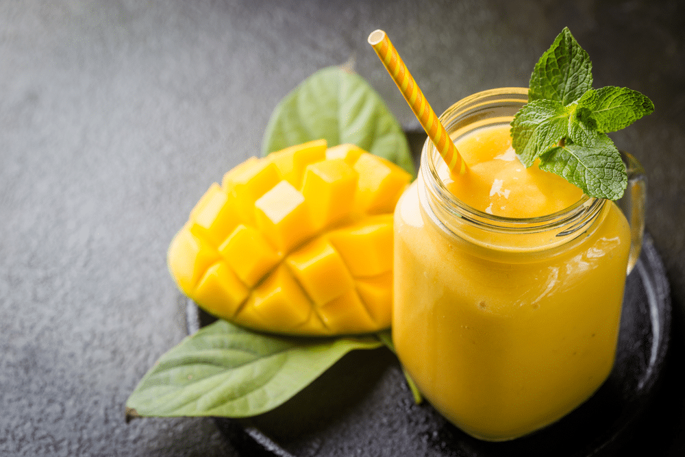 Refreshing and healthy mango smoothie in a glass with fresh fruit over stone background