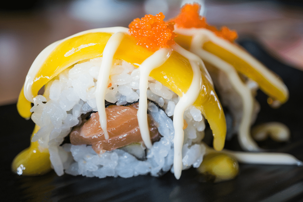 Salmon sushi roll with mango fruit japanese food style on black ceramic dish