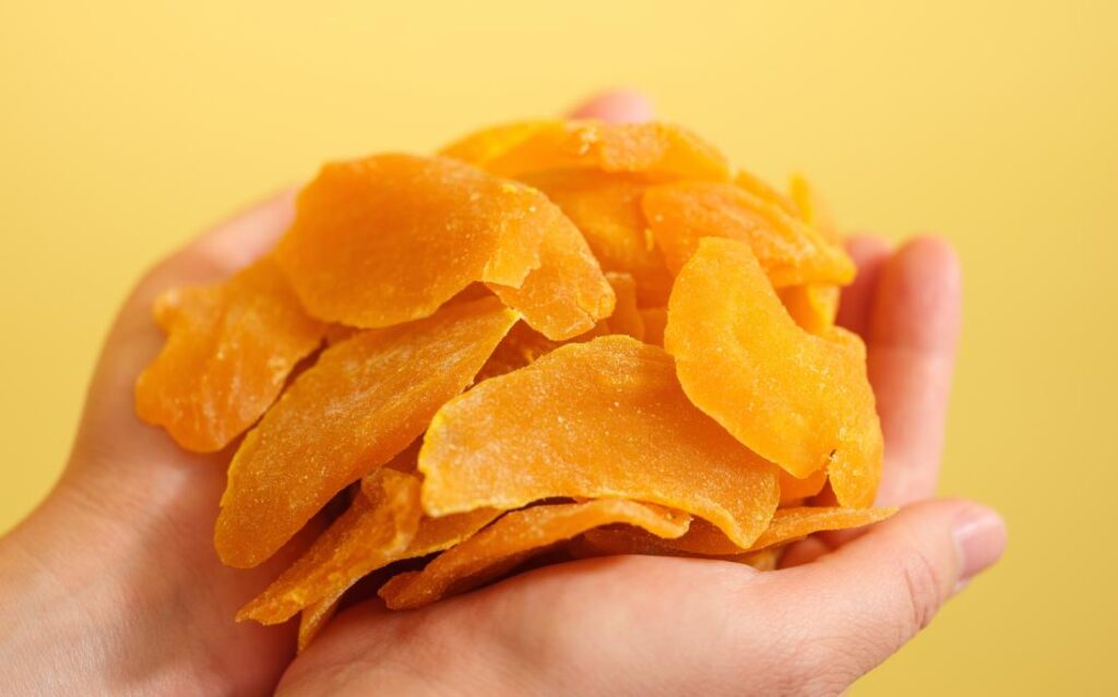 Hands holding a pile of dried mango slices against a yellow background