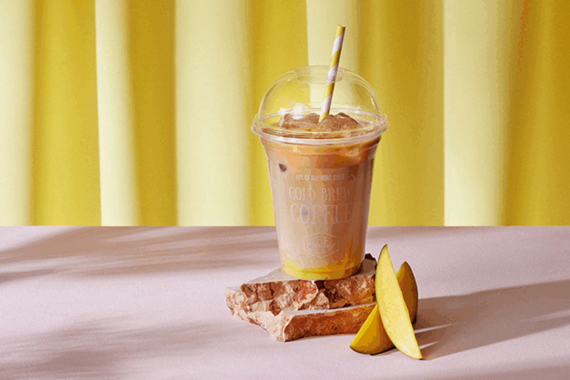 Iced mango cold brew coffee with straw served on stone with mango slices Iced mango cold brew coffee with straw served on stone with mango slices