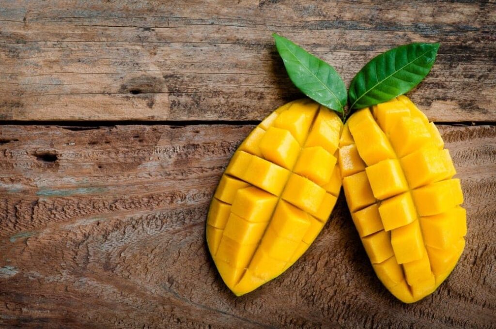 Two halves of a cubed mango with green leaves arranged on a rustic wooden surface