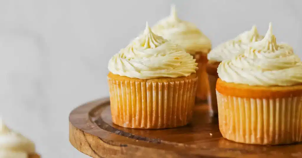 Close up of mango cupcakes with swirled buttercream frosting on a wooden cake stand Close up of mango cupcakes with swirled buttercream frosting on a wooden cake stand