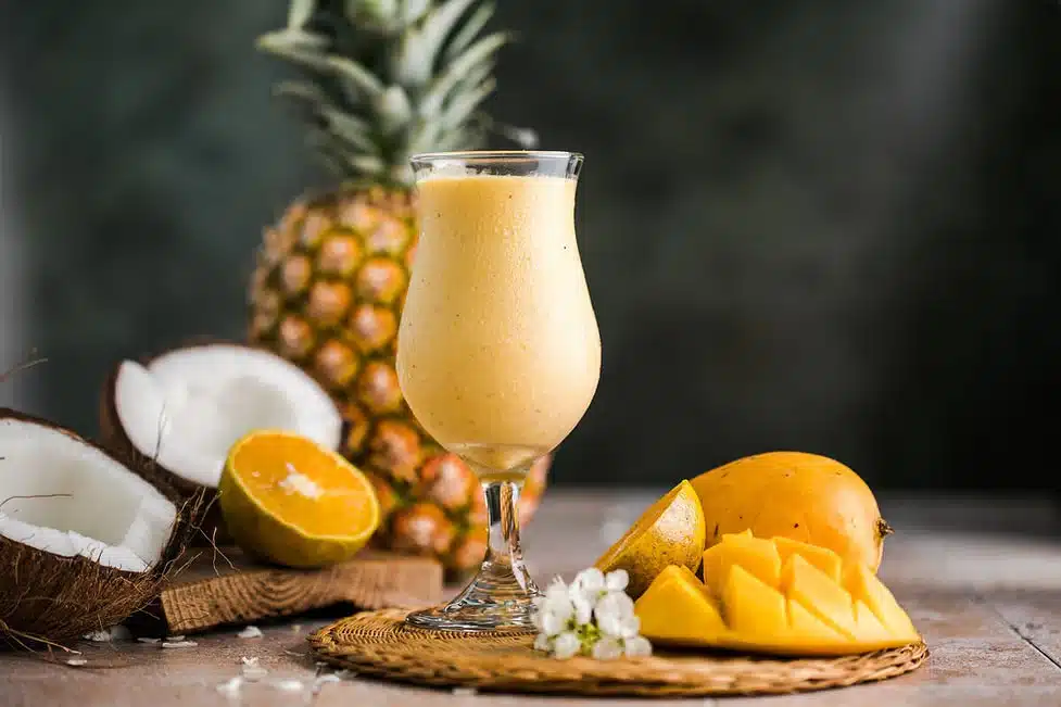 Glass of tropical mango smoothie surrounded by mango coconut and pineapple