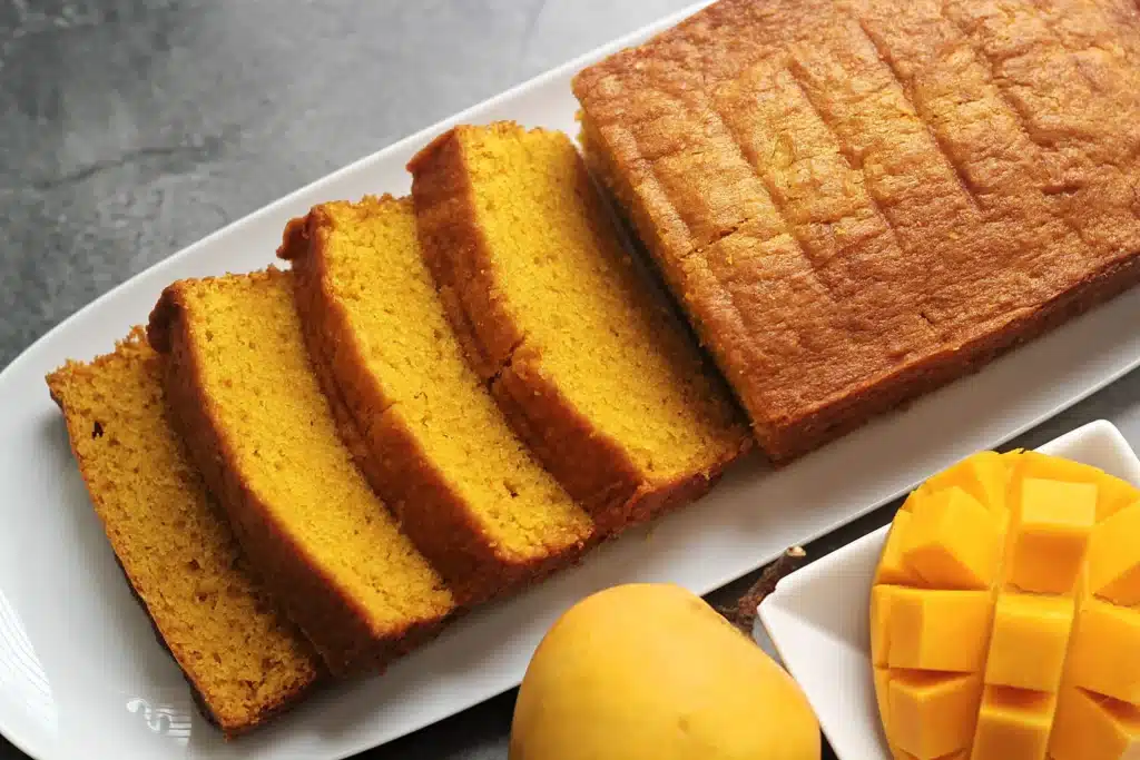 Sliced mango cake with a whole mango on the side and cubes of mango on a plate Sliced mango cake with a whole mango on the side and cubes of mango on a plate