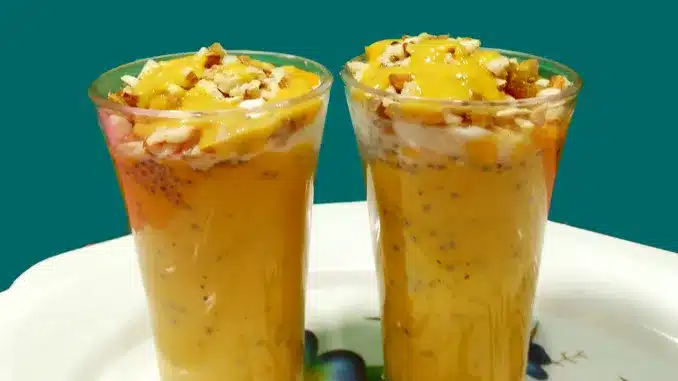 Two glasses of thick mango shake topped with nuts and mango pieces