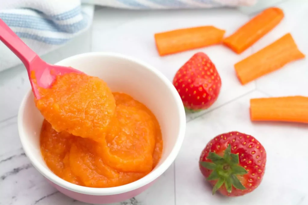 A bowl of smooth mango puree for babies served with carrot sticks and strawberries on the side A bowl of smooth mango puree for babies served with carrot sticks and strawberries on the side