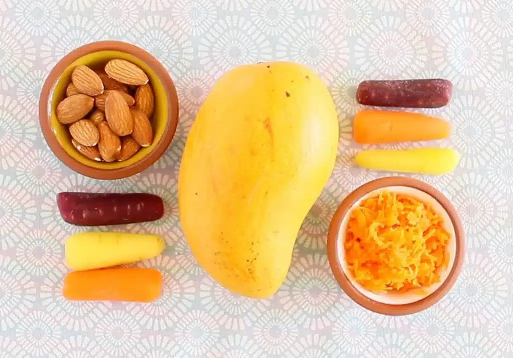 A mango surrounded by bowls of almonds grated carrots and colorful carrot sticks arranged for a baby food recipe A mango surrounded by bowls of almonds grated carrots and colorful carrot sticks arranged for a baby food recipe